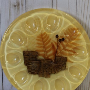 Peut inclure: Un plat jaune en forme d'œuf avec 12 compartiments individuels. Le plat a un motif de fougère pressée et de baies séchées au centre.