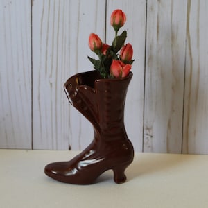 May include: A brown ceramic boot-shaped vase with a bouquet of pink flowers.