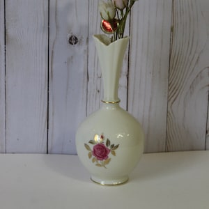May include: A white ceramic vase with a gold rim and a pink rose design. The vase is filled with a bouquet of pink and white silk roses.