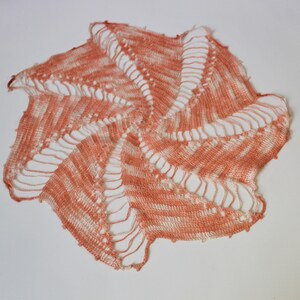 May include: A crocheted doily in a peach and white color scheme. The doily has a spiral design with a scalloped edge.