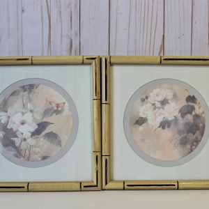May include: Two framed prints with a light brown bamboo frame. The prints feature a circular design with a watercolor-style floral motif. One print features white flowers and a butterfly, while the other features pink flowers.
