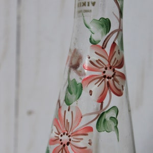 May include: A clear glass vase with a floral design. The vase is decorated with pink and white flowers and green leaves. The vase has a label that reads "VIKING".