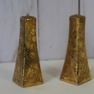 May include: A pair of gold salt and pepper shakers with a floral pattern.
