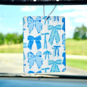 May include: A white car air freshener with a blue and white bow pattern.