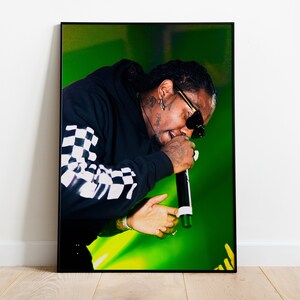 May include: A black hoodie with a white and black checkered sleeve, worn by a person with sunglasses singing into a microphone on a green stage.