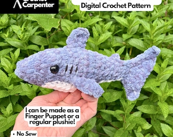 May include: A crocheted shark plushie in shades of blue and purple, with a white belly and black eyes. The text "Bruce the Shark Digital Crochet Pattern" is displayed above the shark. The text "I can be made as a Finger Puppet or a regular plushie!" is also visible.