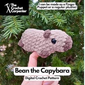 May include: A crocheted capybara plushie in shades of tan and brown, with a black eye. The text "Bean the Capybara" and "Digital Crochet Pattern" are displayed. The image also includes the text "I can be made as a Finger Puppet or a regular plushie!"