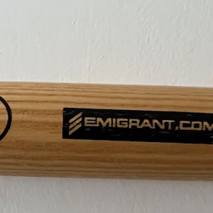 May include: A wooden baseball bat with a black and white New York Yankees logo, a black label with the text "EMIGRANT.COM", and a black oval label with the text "PRO Louisville Slugger Louisville, Kentucky Made in USA".