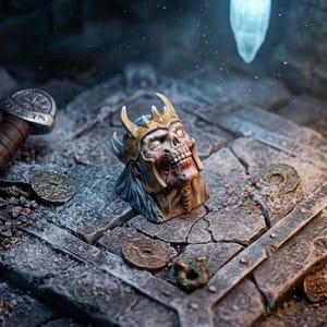 May include: A detailed miniature figurine of a skeletal king wearing a golden crown, positioned on a cracked stone floor alongside a metallic sword with a brown leather-wrapped handle and several scattered circular coins in a dimly lit setting.