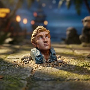 May include: A sculpted bust of a person with blonde hair, light skin, and blue eyes, wearing a blue collared jacket. The figure is positioned partially submerged in a small pile of light brown sand and small pebbles on a stone surface.