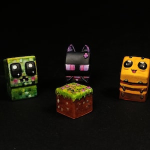 Peut inclure: Quatre figurines colorées en forme de cube sur une surface noire. Les figurines comprennent un Creeper vert, un Enderman noir, un bloc de terre avec de l'herbe et une abeille jaune. Chaque figurine a un design et une expression faciale uniques.