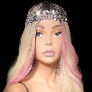 May include: A mannequin with long blonde hair with pink highlights wearing a black velvet top and a silver sequined headband.