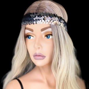 May include: A black and silver sequin headband. The headband is worn on a mannequin with blonde hair and blue eyes. The mannequin is wearing a black velvet top with spaghetti straps. The background is black.