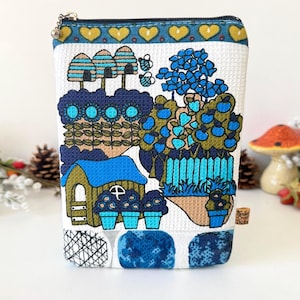 May include: A rectangular fabric zipper pouch with a white textured background featuring a colorful print of beehives, blue flowers, a small house, and a fence. The top border has a pattern of yellow hearts on a teal band with a silver zipper.