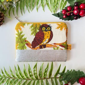 May include: A rectangular coin purse with a silver base and a yellow zip. The main body features a brown and yellow owl perched on a branch, set against a cream background with green and yellow leaves.