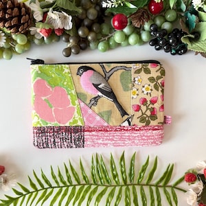 May include: A rectangular patchwork coin purse with a black zip. The design features a bird perched on a branch, pink flowers, and strawberry and floral patterns. The purse is trimmed with a pink and red patterned fabric.