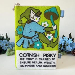 May include: A lime green zippered pouch featuring a printed illustration of a figure in a blue tunic and green hat holding a large mushroom. The bottom white section includes the text: CORNISH PISKY THE PISKY IS CARRIED TO ENSURE HEALTH, WEALTH, HAPPINESS AND SUCCESS.