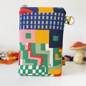 May include: A rectangular fabric pouch featuring a vibrant geometric pattern in shades of blue, yellow, green, pink, and red. The pouch includes a silver metal zipper at the top, a side metal D-ring, and a small yellow fabric tag on the right side.