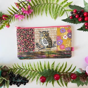 May include: A rectangular, patchwork-style zippered pouch with a pink zipper. The pouch features three fabric panels: floral, owl, and floral patterns. The owl panel has a black and white owl illustration. The pouch is decorated with floral and berry accents.
