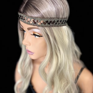 May include: A decorative headband with a row of bronze-colored sequins. The headband is on a mannequin head with blonde and gray hair. The background is black.