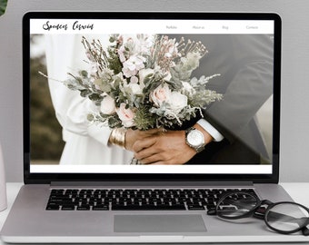 May include: A laptop computer displaying a website for a wedding photographer. The website has a menu bar with the words "Portfolio", "About Us", "Blog", and "Contact". The website's background image shows a bride and groom holding a bouquet of flowers.
