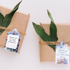 May include: Two gift boxes wrapped in brown paper with twine and topped with green leaves. Each box has a gift tag with a floral design and a message that reads "Jehovah loves you and so do we! Here's a little something for you!"