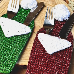 May include: Two crocheted Christmas stocking-shaped cutlery holders. One is green with a white pom-pom and the other is red with a white pom-pom. Both holders have a white crocheted triangle inside.