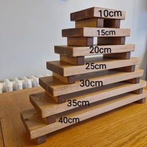 May include: A set of wooden display risers in various sizes. The risers are made of light and dark brown wood, with the dimensions labeled in centimetres: 10cm, 15cm, 20cm, 25cm, 30cm, 35cm, and 40cm. Each riser has a rectangular top and is supported by four small legs.