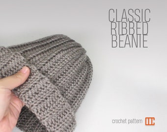 Könnte beinhalten: Eine graue Häkelmütze mit Rippenmuster. Die Mütze ist in der Hälfte gefaltet und wird von einer Hand gehalten. Der Text "CLASSIC RIBBED BEANIE" befindet sich über der Mütze und der Text "crochet pattern" unter der Mütze.