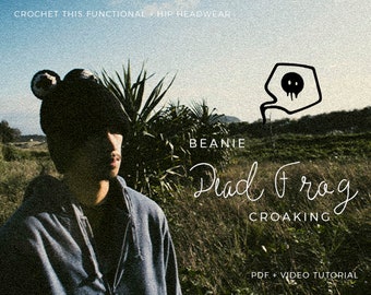 May include: A black beanie with a distinctive design, worn by a person in a blue hoodie. The image features the text "Dead Frog Croaking" and "Crochet this functional hip headwear". A speech bubble with a skull graphic is also visible.