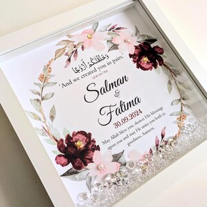 May include: A white framed print with a floral design in shades of pink and burgundy. The print features an Arabic quote, "And we created you in pairs."  The names Salman & Fatima and the date 30.09.2024 are also included. The print is decorated with clear rhinestones.