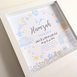 May include: A white frame with a blue and yellow watercolor illustration of stars, a crescent moon, a rainbow, and a sun. The name "Hamzah" is written in Arabic calligraphy and the date "24.09.2024" is written below. The frame is filled with clear crystals. The text "أعيدكَ بِكَلِمَاتِ اللَّهِ التَّامَّةِ مِنْ كُلِّ شَيْطَانٍ وَهَامَّةٍ وَمِن كُلِّ عَيْنٍ لَامَّة" is written in Arabic script. The text "I seek refuge for you with Allah's perfect words from every devil, poisonous creature and every evil eye." is written in English below the Arabic text.