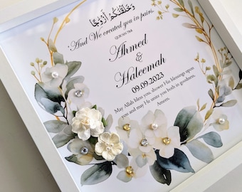 May include: White framed art print featuring floral and leaf accents, with the names "Ahmed & Haleemah" and the date 09.09.2023. The print includes text in English and Arabic script, with decorative embellishments.