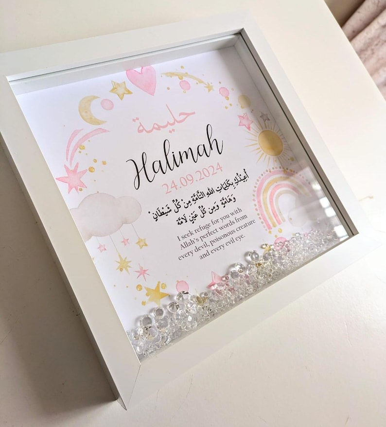 May include: A white frame with a pink and gold design featuring a name, date, and Arabic text. The frame is filled with clear glitter.