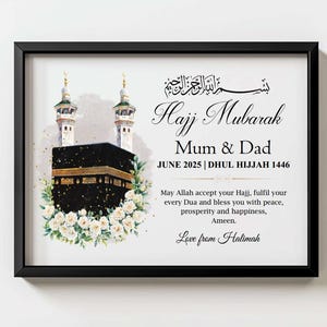 May include: A framed print with the words "Hajj Mubarak Mum & Dad" and the date June 2025. The image features a watercolor illustration of the Kaaba, surrounded by white flowers, and two minarets. The frame is black.