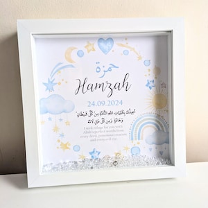 May include: A white framed picture with a blue and yellow watercolor design featuring stars, clouds, a rainbow, and a sun. The name "Hamzah" is written in a decorative font with the date "24.09.2024" below it. The picture also includes an Arabic inscription and its English translation.