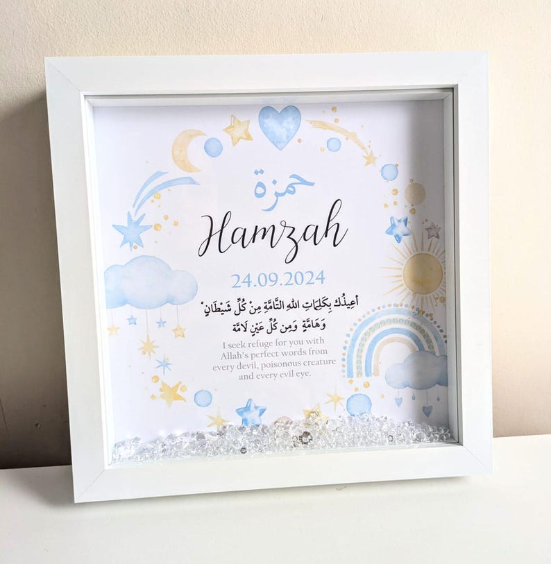 May include: A white framed picture with a blue and yellow watercolor design featuring stars, clouds, a rainbow, and a sun. The name "Hamzah" is written in a decorative font with the date "24.09.2024" below it. The picture also includes an Arabic inscription and its English translation.