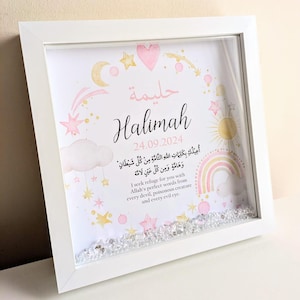 May include: A white framed picture with a pink and gold design. The picture includes the name "Halimah" and the date "24.09.2024". The picture also includes a rainbow, stars, and a cloud with Arabic text. The text in English reads: "I seek refuge for you with Allah's perfect words from every devil, poisonous creature and every evil eye."