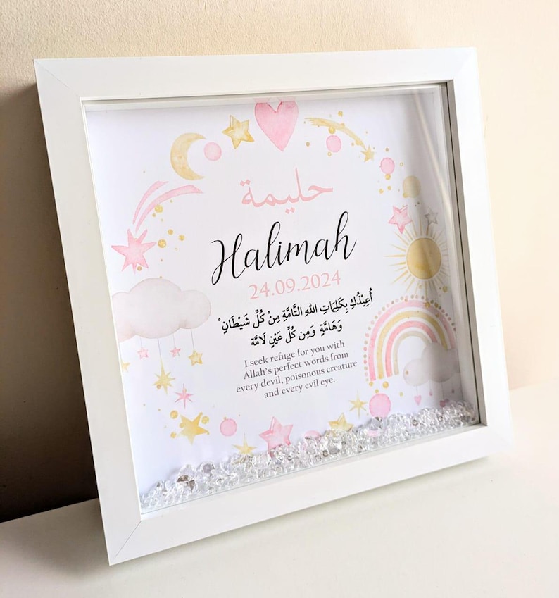 May include: A white framed picture with a pink and gold design. The picture includes the name "Halimah" and the date "24.09.2024". The picture also includes a rainbow, stars, and a cloud with Arabic text. The text in English reads: "I seek refuge for you with Allah's perfect words from every devil, poisonous creature and every evil eye."