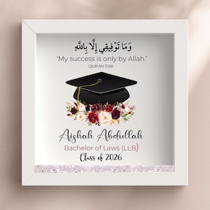 May include: A square white frame containing a graduation print with a black mortarboard cap resting on a cluster of burgundy and white flowers. The text reads: 'My success is only by Allah.', 'Aishah Abdullah', 'Bachelor of Laws (LLB)', and 'Class of 2026'.