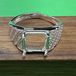 May include: A silver ring with a square setting for a gemstone. The ring has a textured band with diagonal lines.