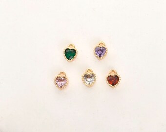 May include: Five gold heart-shaped charms with different colored gemstones. The charms have a beaded border and are perfect for jewelry making.