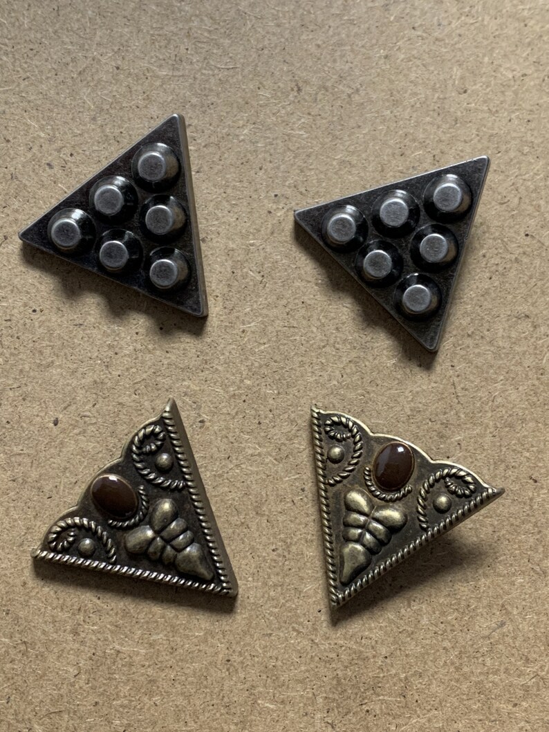 May include: Four metal triangle corner protectors. Two are silver with a hammered finish and six round studs. Two are gold with a decorative design and a brown stone in the center.
