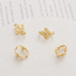 May include: Four gold-toned metal jewelry connectors. Two connectors feature a delicate floral design with a small clear rhinestone in the center. The other two connectors are simple oval shapes.