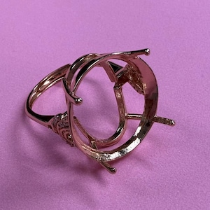 Può includere: Una montatura per anello in oro rosa con una grande lunetta ovale. La montatura ha un design delicato con una piccola fila di pietre sulla fascia.