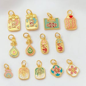Puede incluir: Una colección de colgantes dorados con diversos diseños, incluyendo motivos florales, geométricos y simbólicos. Los colgantes presentan detalles de esmalte de colores en rosa, azul y verde, algunos con caracteres chinos. Cada colgante tiene un pequeño lazo.