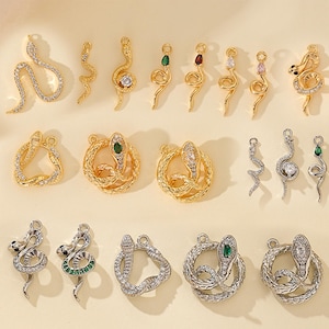 May include: A selection of gold and silver snake charms. The charms feature intricate designs, some with clear or coloured gemstones and sparkling crystals. The snake charms vary in size and shape, ideal for jewellery making and crafting.