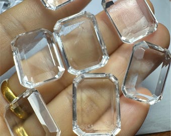 以下が含まれることがあります： 8つの透明なファセットカットの四角い水晶の集合。水晶は手に置かれ、一部は重なっている。