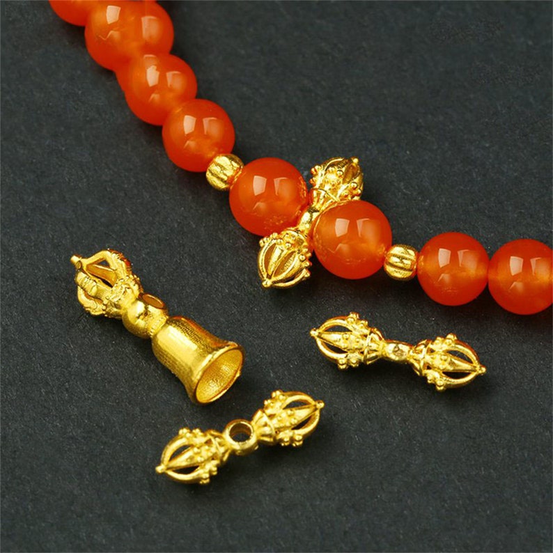 May include: A gold-toned bracelet with orange beads and decorative gold charms. The charms are in the shape of a traditional Tibetan prayer wheel.
