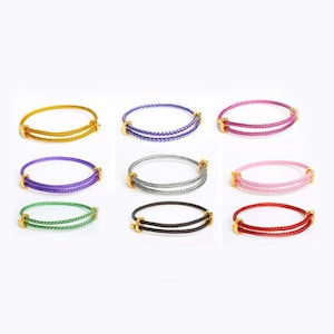 May include: Nine colorful bangles in gold, purple, pink, green, black, red, silver, blue, and yellow. Each bangle features a braided design and gold-colored accents. The bangles are displayed on a white background.